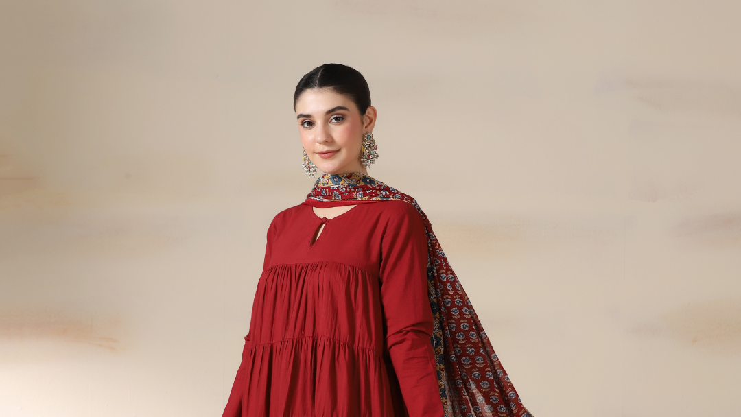 Woman wearing a red traditional outfit with a patterned scarf on a beige background